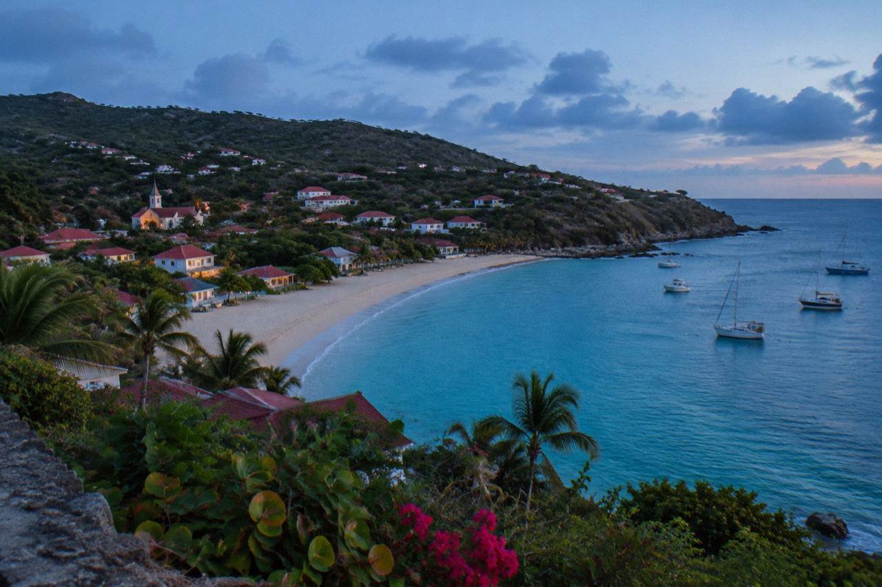 A sandy beach curving along a green hillside on a Caribbean island with calm turquoise water
