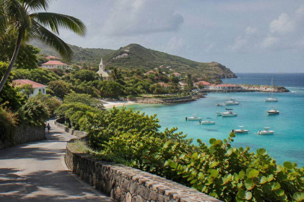 A coastal road winding past green hills with a glimpse of turquoise sea