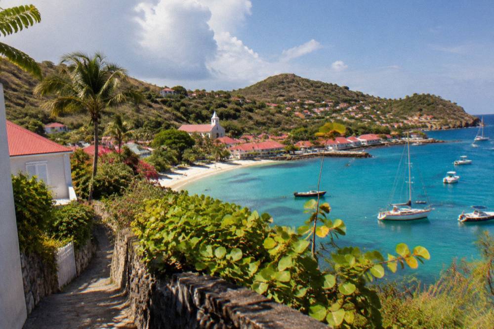 White houses with red roofs on a green hillside above a Caribbean bay