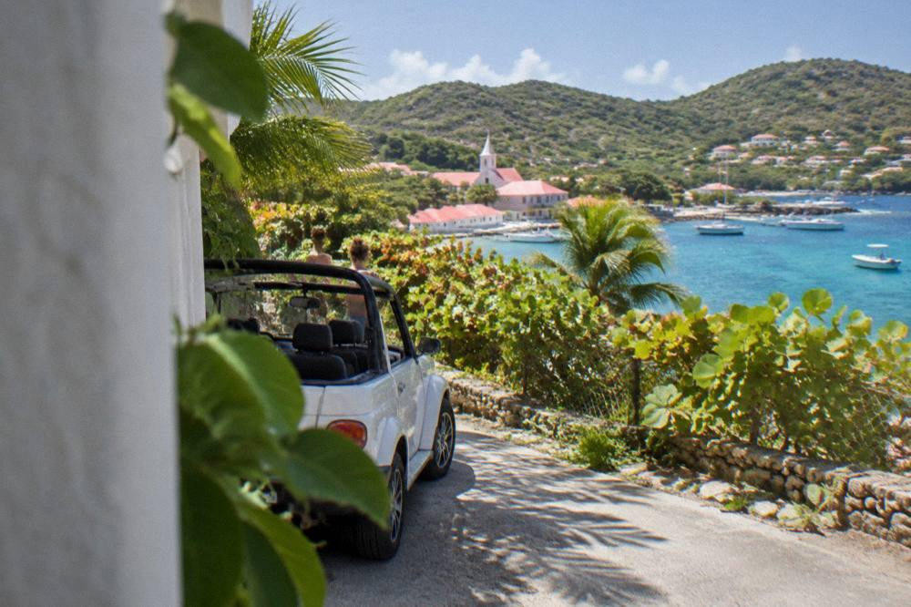 A small open-top rental car parked beside a narrow road with tropical vegetation