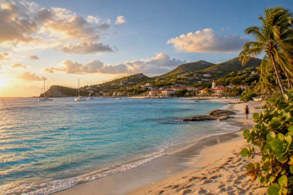 A quiet Caribbean beach at golden hour with calm water and scattered clouds