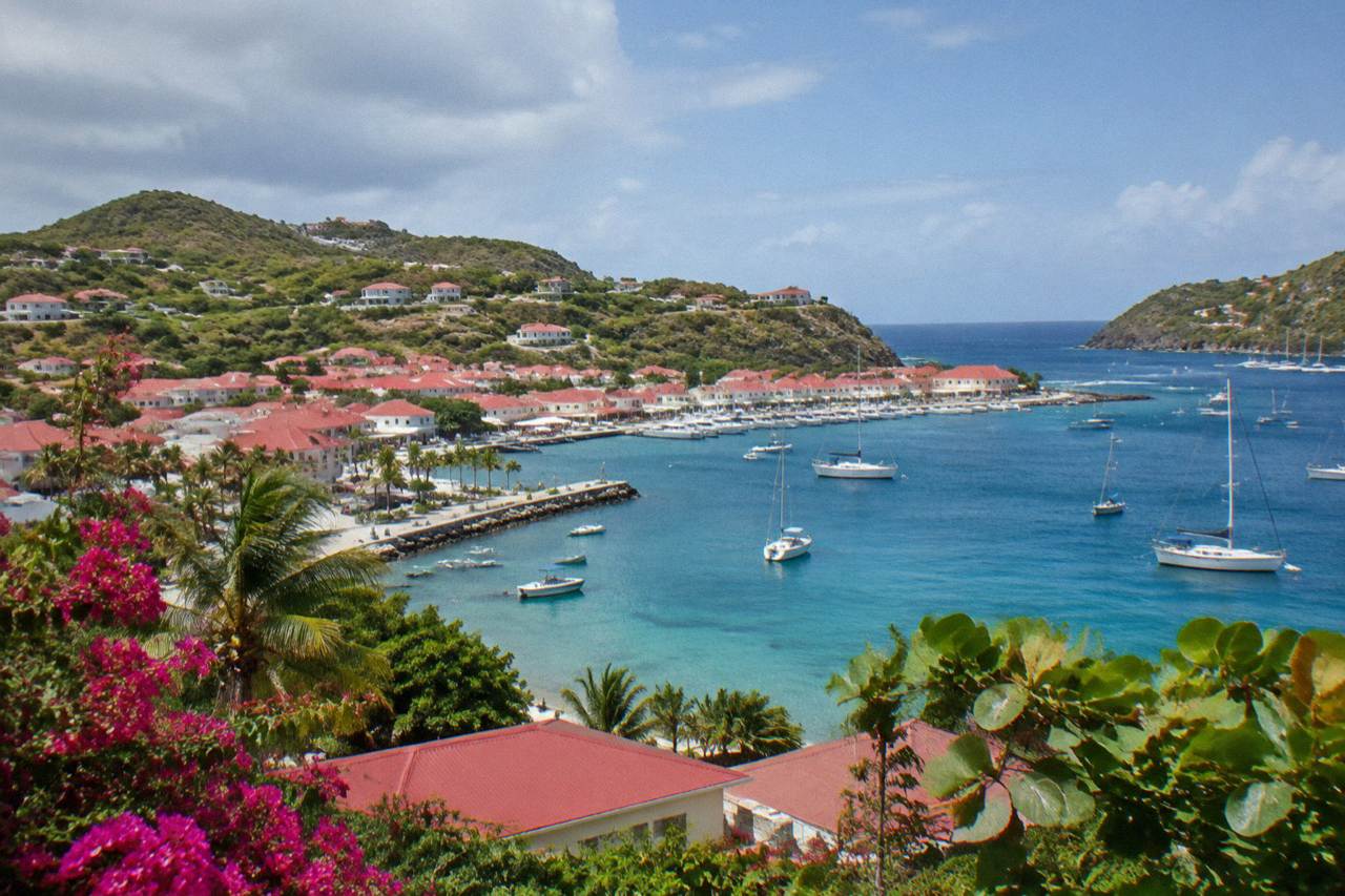 Aerial view of a small Caribbean island with green hills, red rooftops and turquoise bays