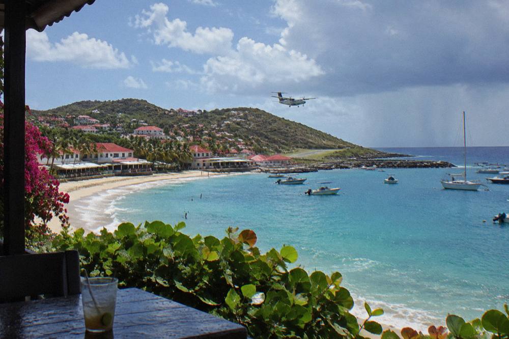A small turboprop aircraft flying low over a hill toward a coastal runway