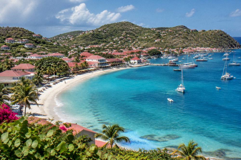 An aerial view of a beach town curving around a bay with hills behind