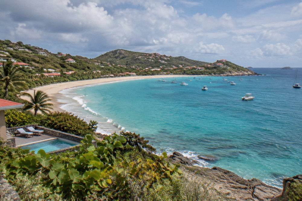 A long open sandy bay backed by low green vegetation under a partly cloudy sky