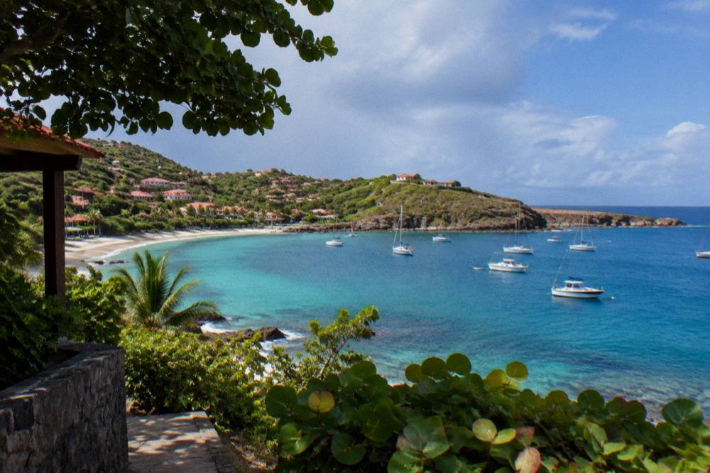 A shallow turquoise bay with a sandy edge and a few moored boats
