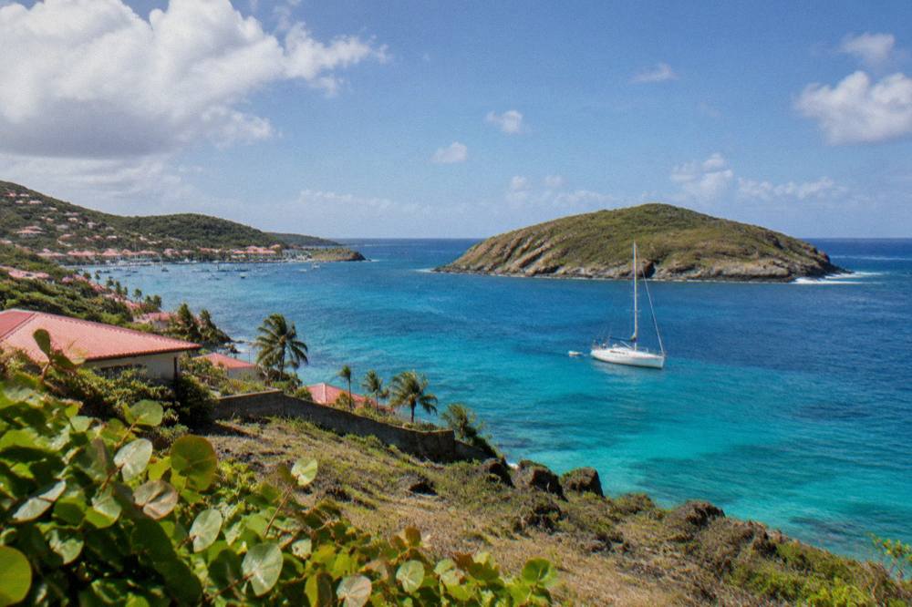 A white sailing boat anchored near a rocky green island with clear water