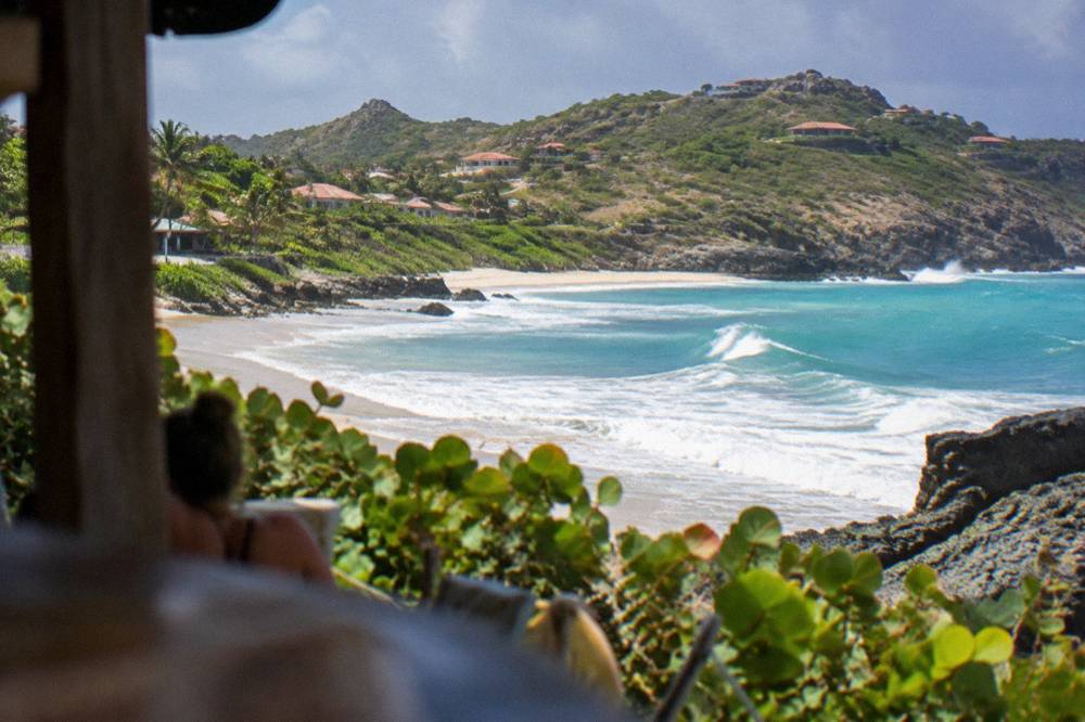 Waves rolling onto a sandy Caribbean beach with scattered low vegetation on the dune line