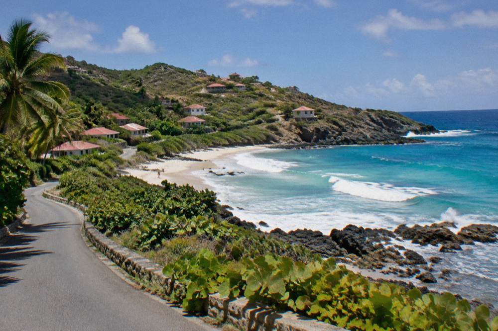 A narrow island road curving between green hillsides with the sea visible in the distance