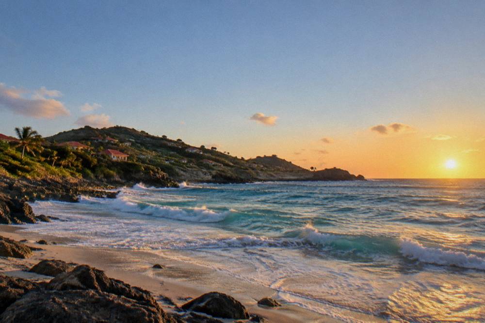 Two sandy coves on a tropical island separated by a low green headland under a clear sky