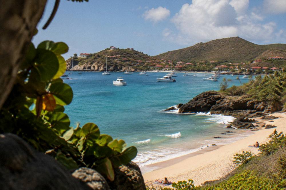 A wide view of a Caribbean bay with scattered white boats on calm turquoise water and hills behind