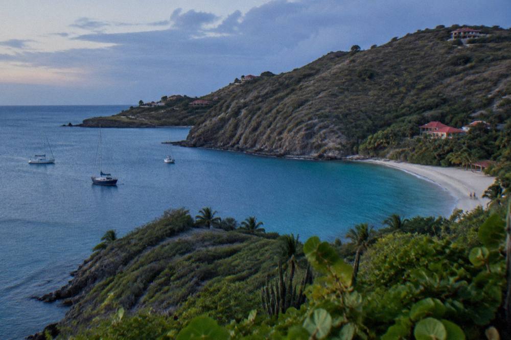 Aerial view of a green headland dropping to a small sandy beach and translucent bay