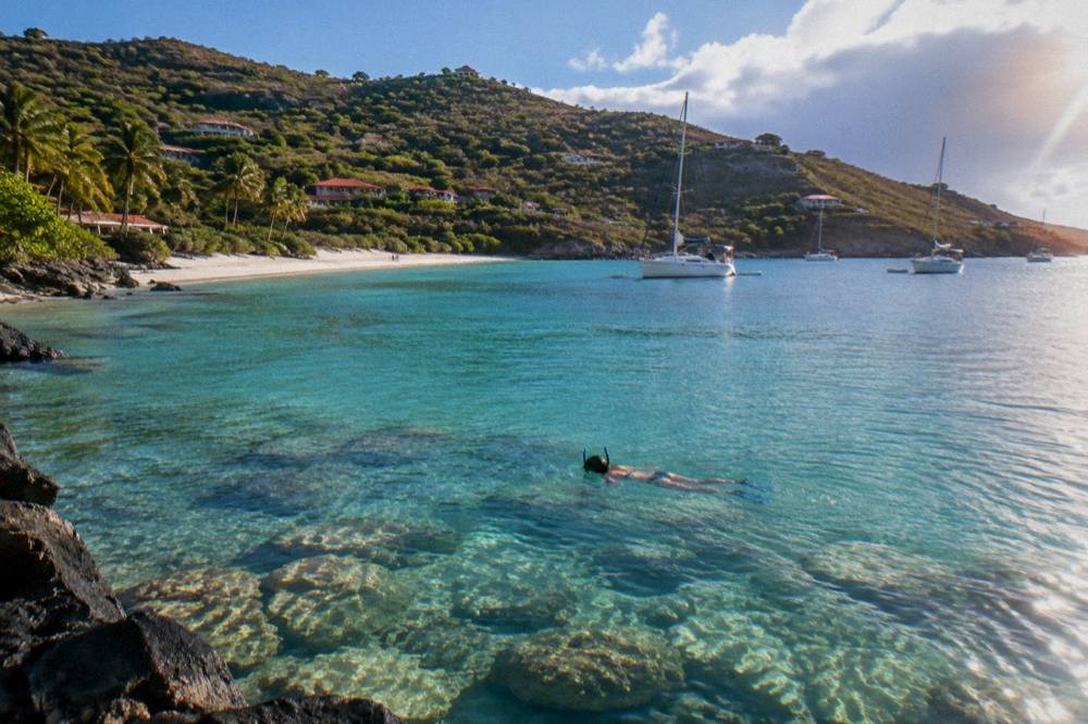 Snorkeller floating above rocks and coral in calm green-blue water