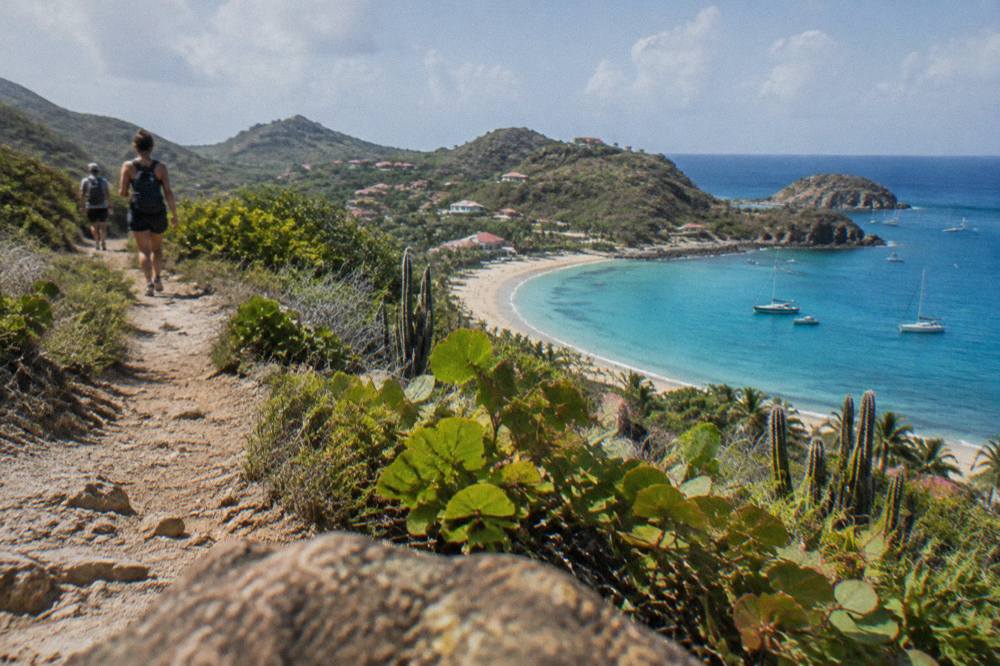 A view of a curved sandy beach below rocky hills seen from a hillside path