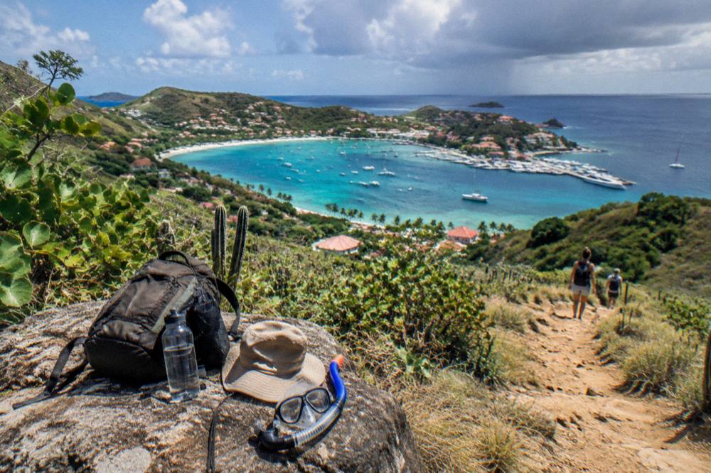 A backpack, water bottle, hat and snorkel mask arranged on a rock