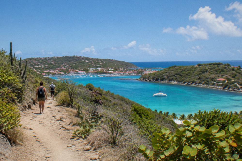 A small sailing catamaran moored in a clear turquoise bay between green headlands