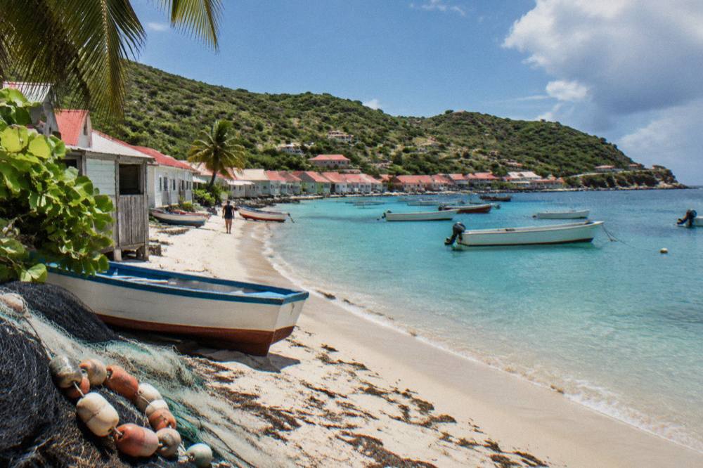 Fishing boats anchored in a small Caribbean bay with green hills rising behind a village