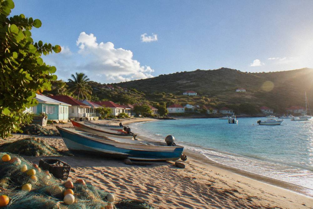 A quiet sandy beach with fishing boats and pastel houses along the shore of a Caribbean village
