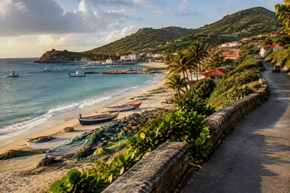A narrow coastal road curving along a green hillside above turquoise Caribbean water