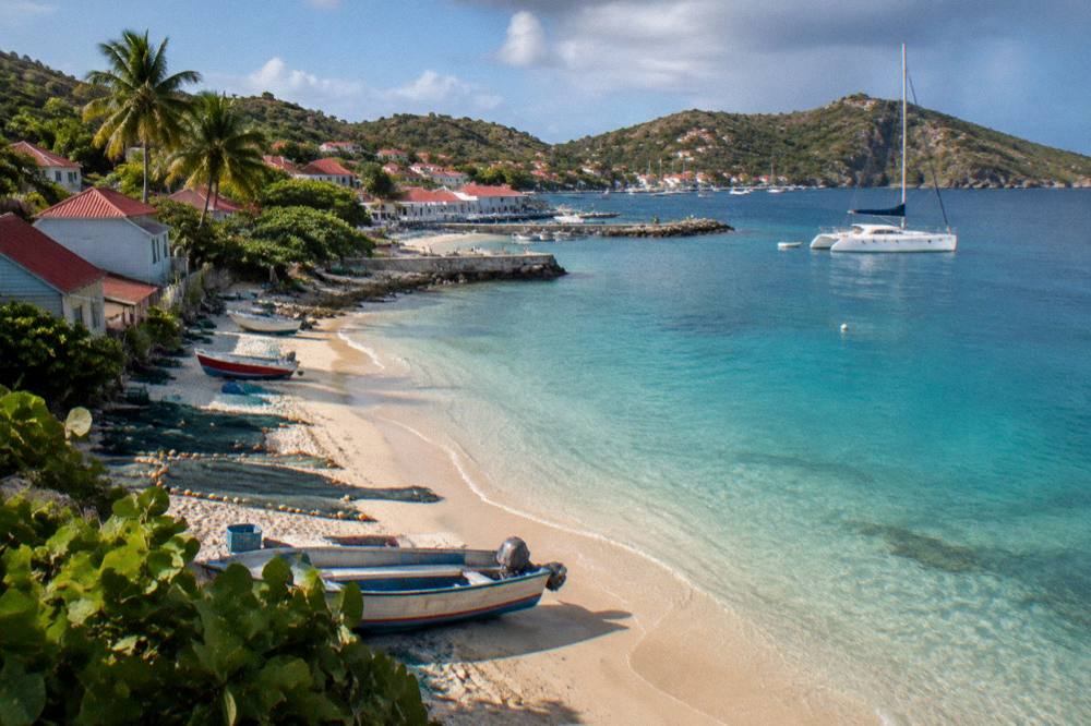 A sailing catamaran anchored in a clear Caribbean bay with green hills in the background