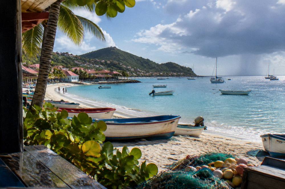 The sun setting over a calm Caribbean sea with silhouetted boats near a village shore