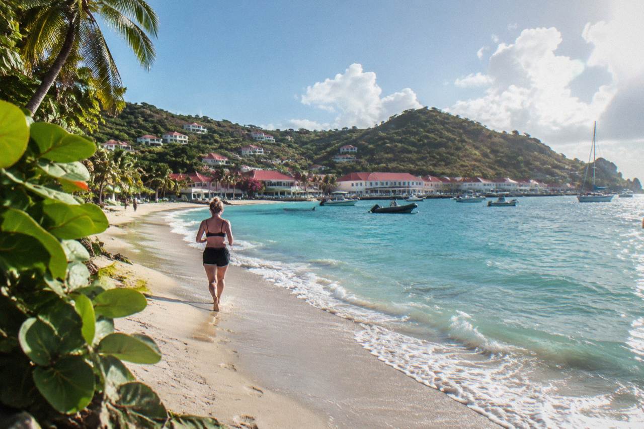 A wide sandy beach curving along a green hillside with turquoise water in St Barts
