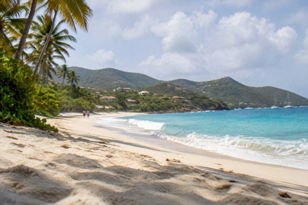 Turquoise water washing onto a broad sandy shore with hills in the background