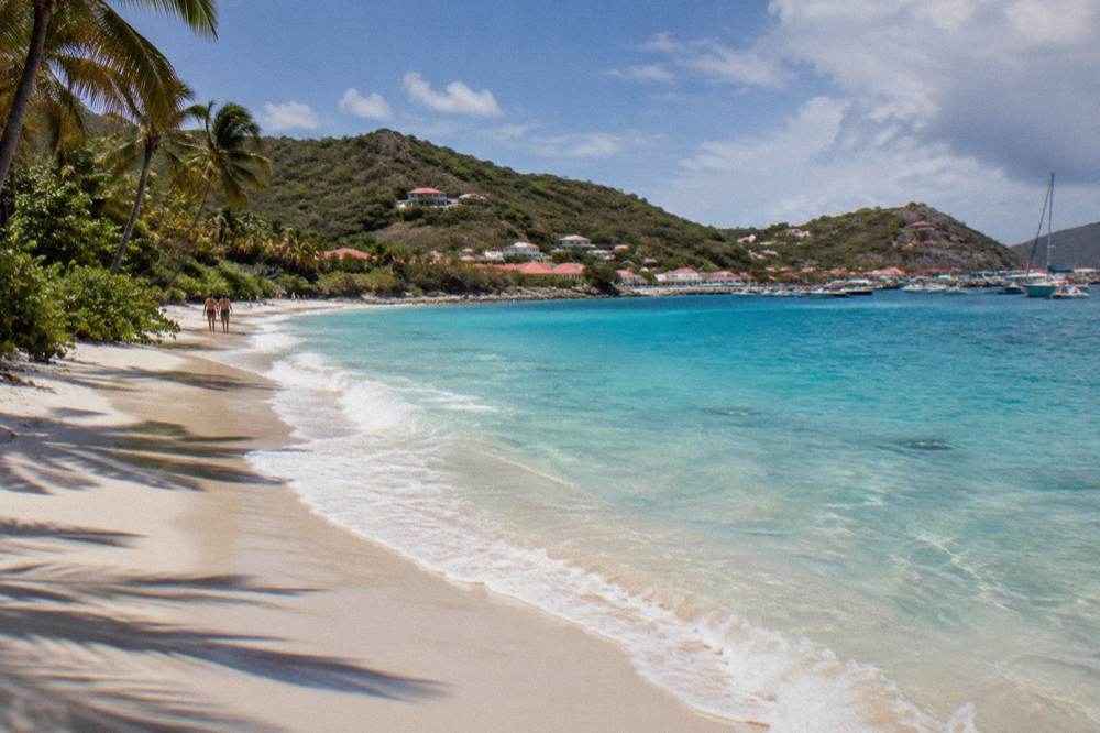 Clear shallow water over sand with tree-covered slopes rising behind the beach
