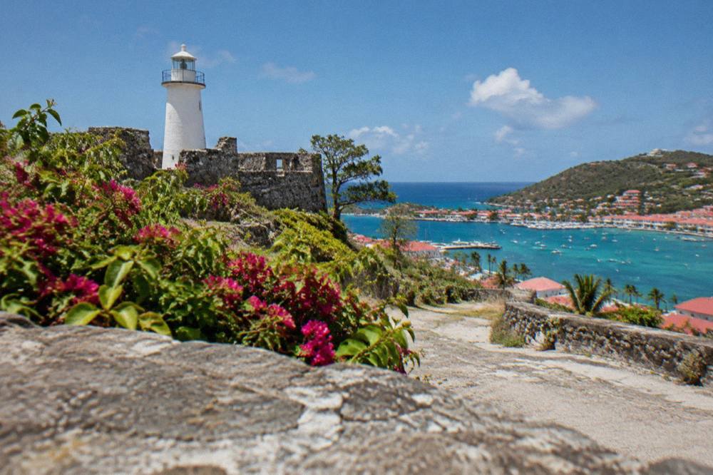 A quiet lane of small houses climbing a steep hill toward a stone tower in a Caribbean town