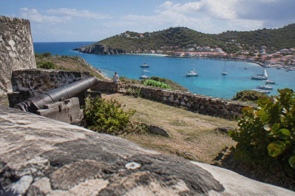Low stone walls of an old fort overlooking sailboats anchored in a Caribbean harbor