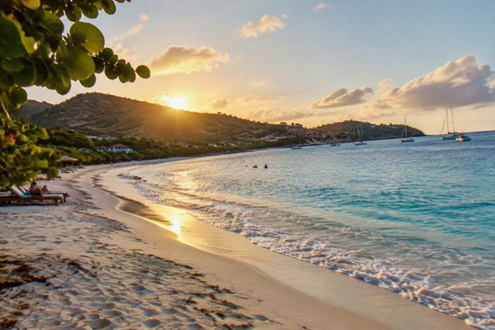 Quiet bay of pale sand beneath green hills with turquoise water