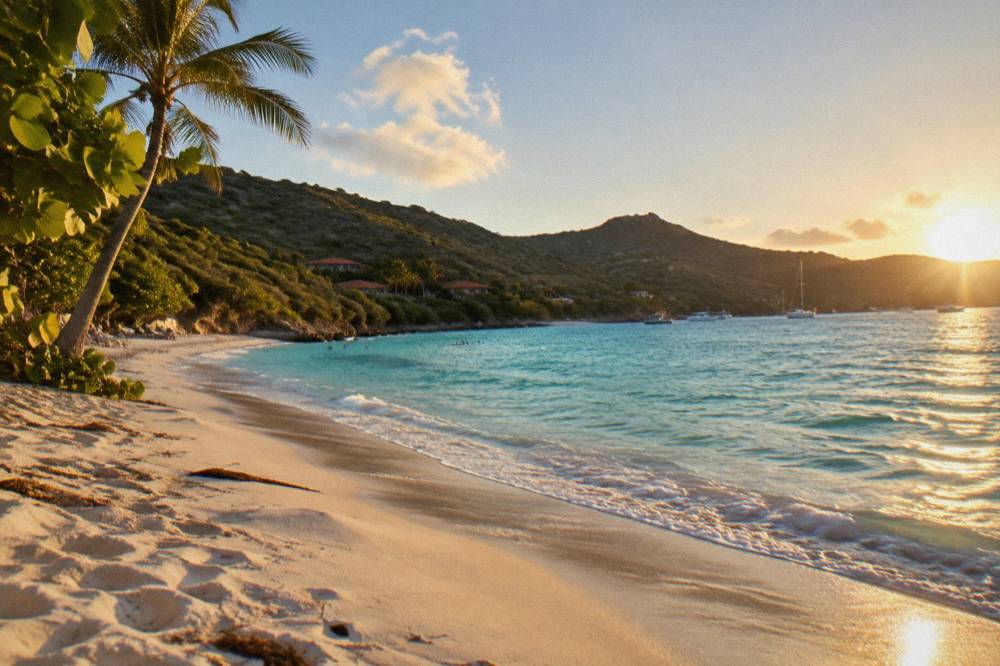 Clear shallow water over sand with green hills rising behind a quiet beach