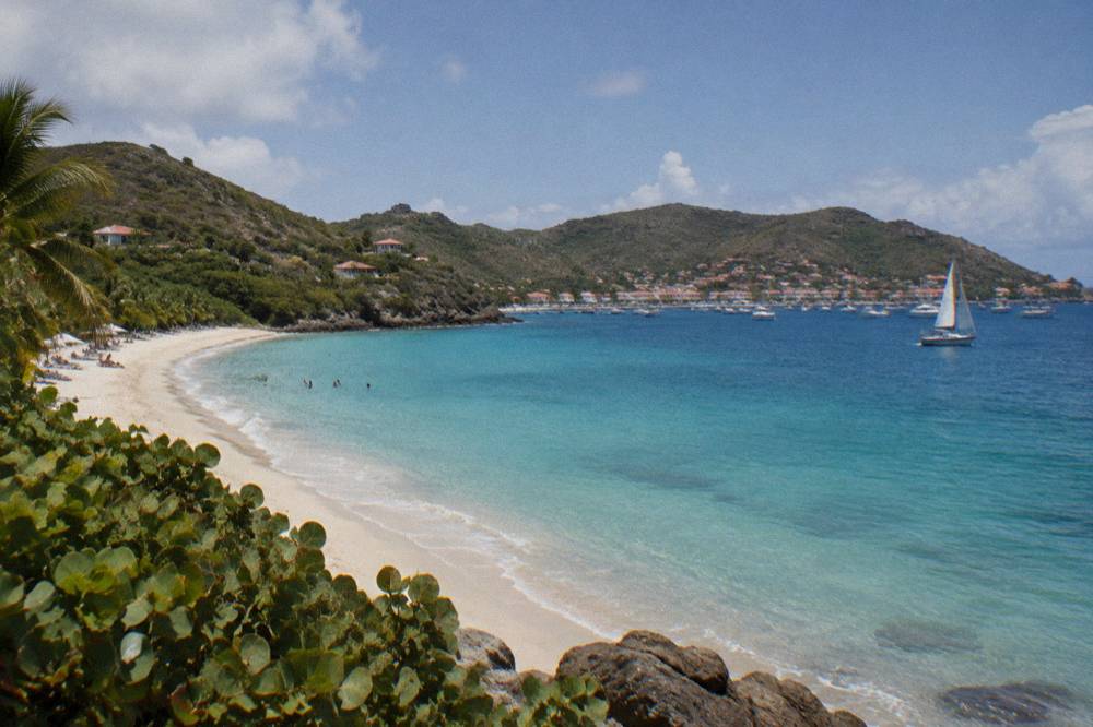 A sailboat on open blue water with a green island coastline in the distance