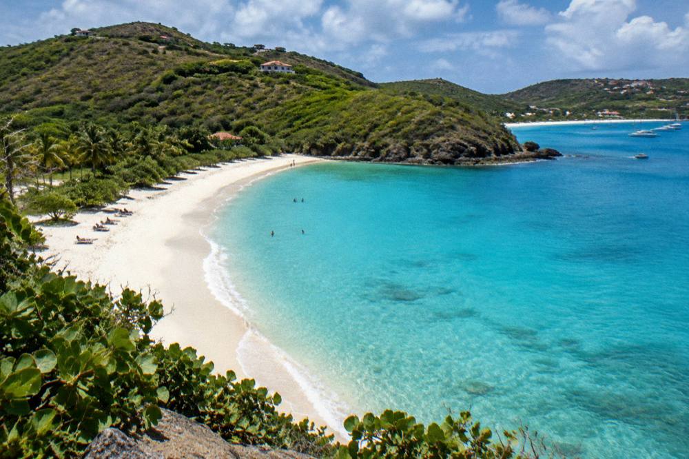 A green headland separating two sandy bays with turquoise water along a coastline
