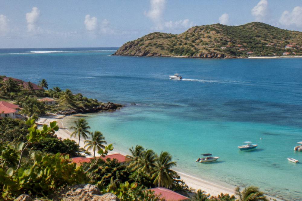 A small boat crossing open blue water toward a green island coastline in morning light