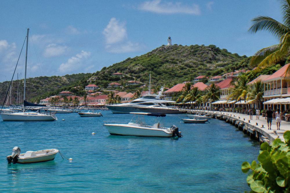 A waterfront promenade in a Caribbean harbour town with moored boats and shopfronts along the quay