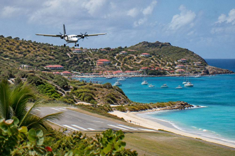 A small turboprop aircraft on a short runway beside a beach and turquoise water