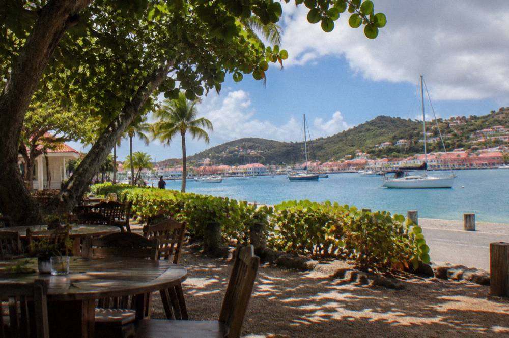 A Caribbean harbor town waterfront with moored sailing yachts and pastel buildings along a quay