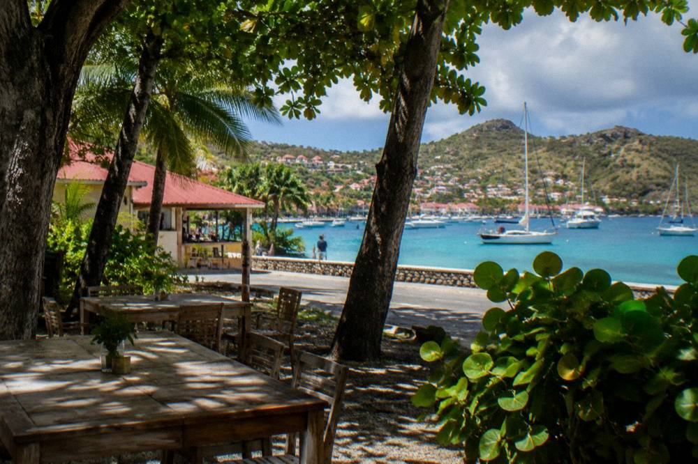 Sailing yachts anchored in a turquoise Caribbean harbor beneath a hillside town