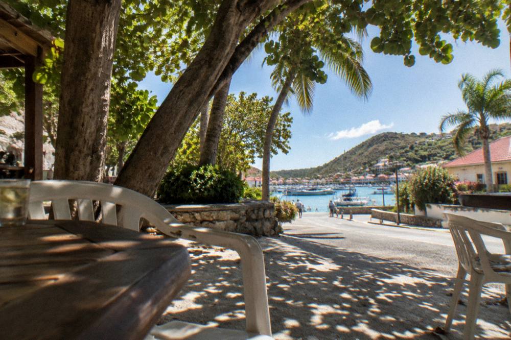 A shaded terrace corner with plastic chairs and a view of a Caribbean street through trees