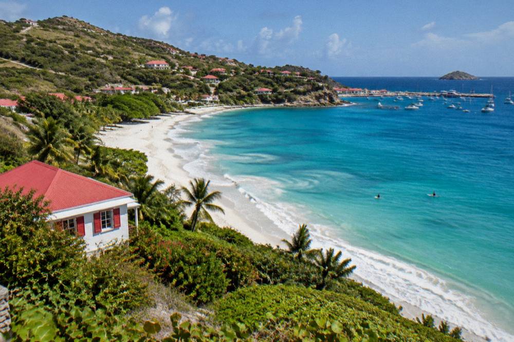 A whitewashed Caribbean villa with a red roof and shutters on a green hillside