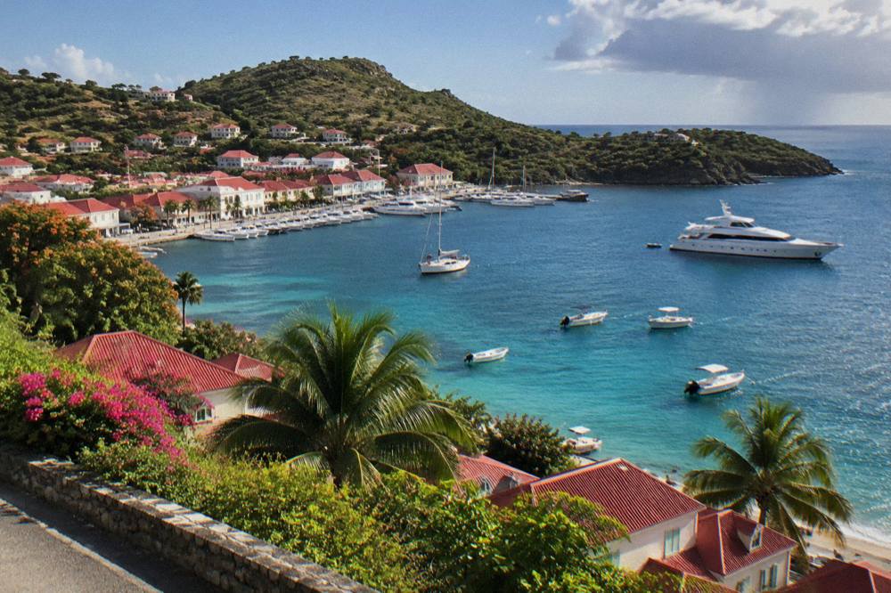 A yacht and small boats on clear water near a green headland in St Barts
