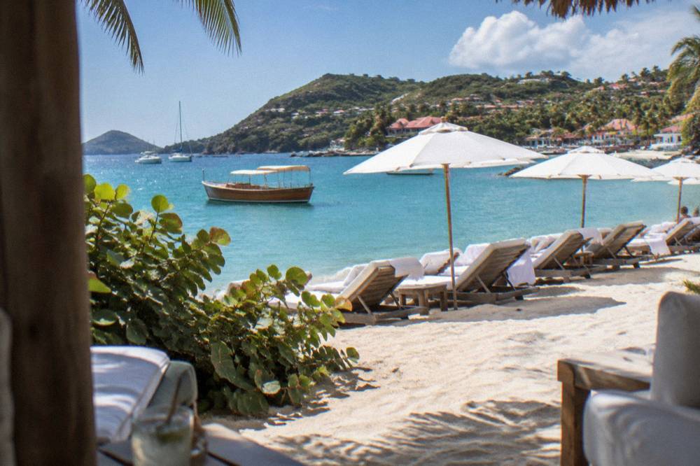 A wooden boat anchored in clear turquoise water near a palm-lined shore