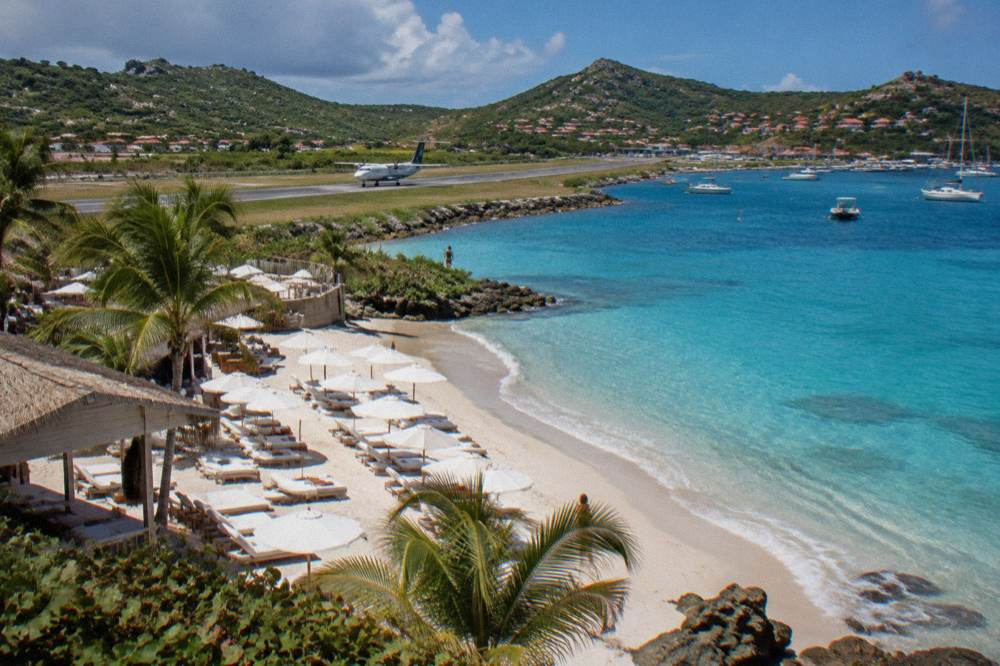 A small turboprop aircraft on a short Caribbean runway with hills behind