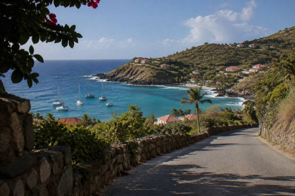 A narrow paved road winding between low stone walls and green hills on a Caribbean island