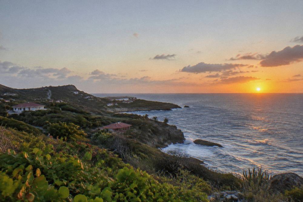 An evening view of the sun setting into the Caribbean Sea seen from a high headland