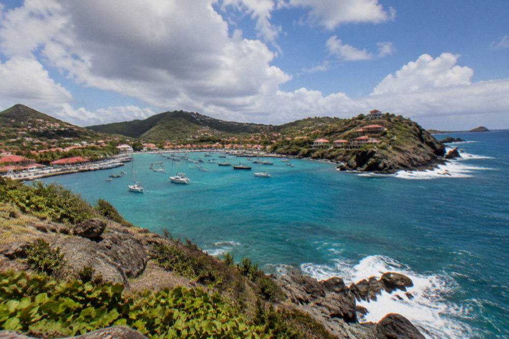 A calm turquoise lagoon behind a line of reef with green hills behind