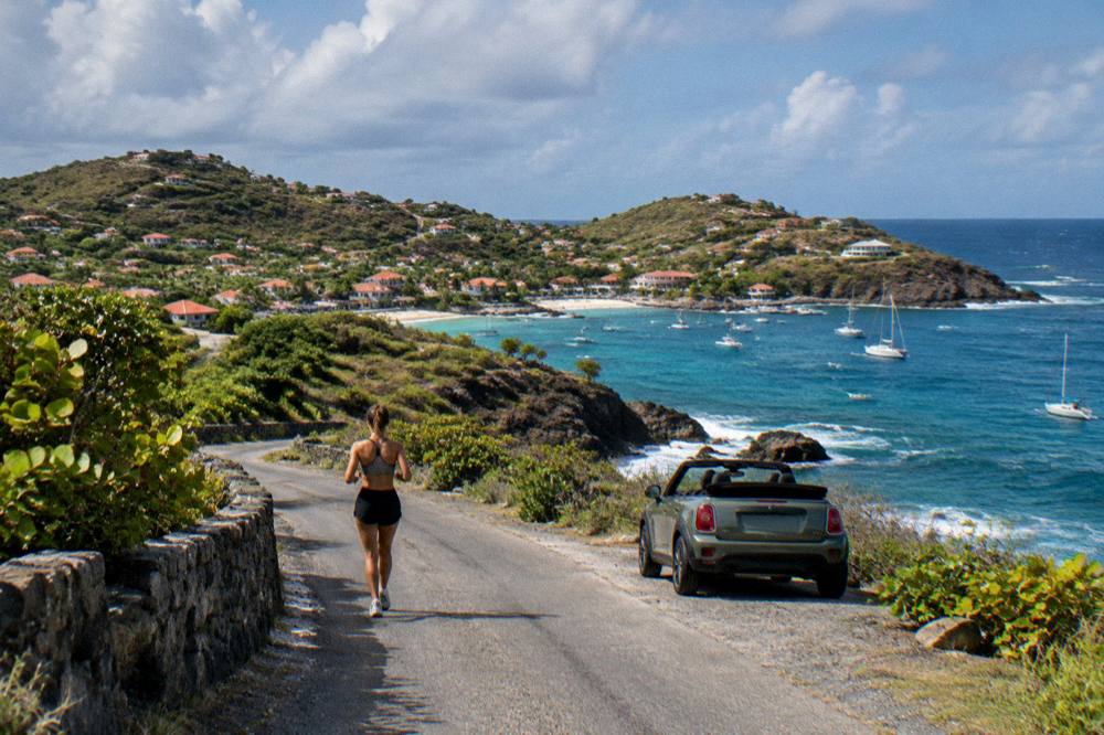 A small open-top car parked on a hillside lane above the sea on an island