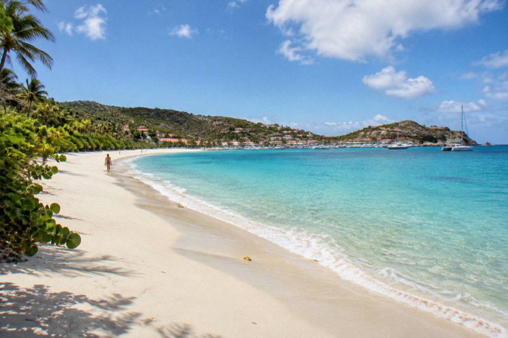 An empty expanse of warm sand curving along a bay with clear shallow water near the shore