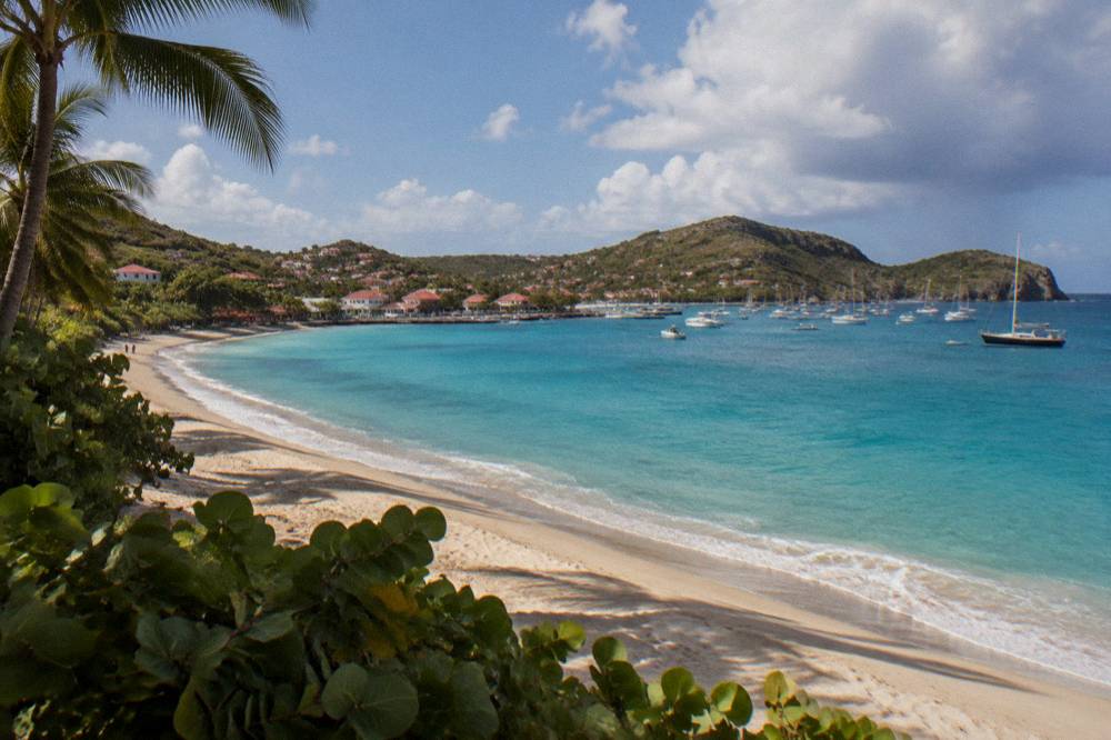 Aerial-style view of a curved sandy bay with turquoise shallows and green hills at each end